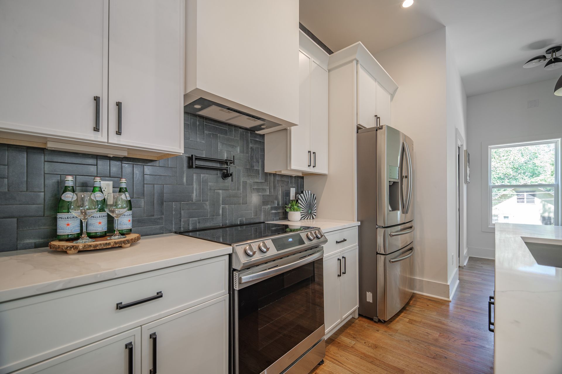 Modern kitchen with white cabinets, stainless steel appliances, dark backsplash, and wooden floors.