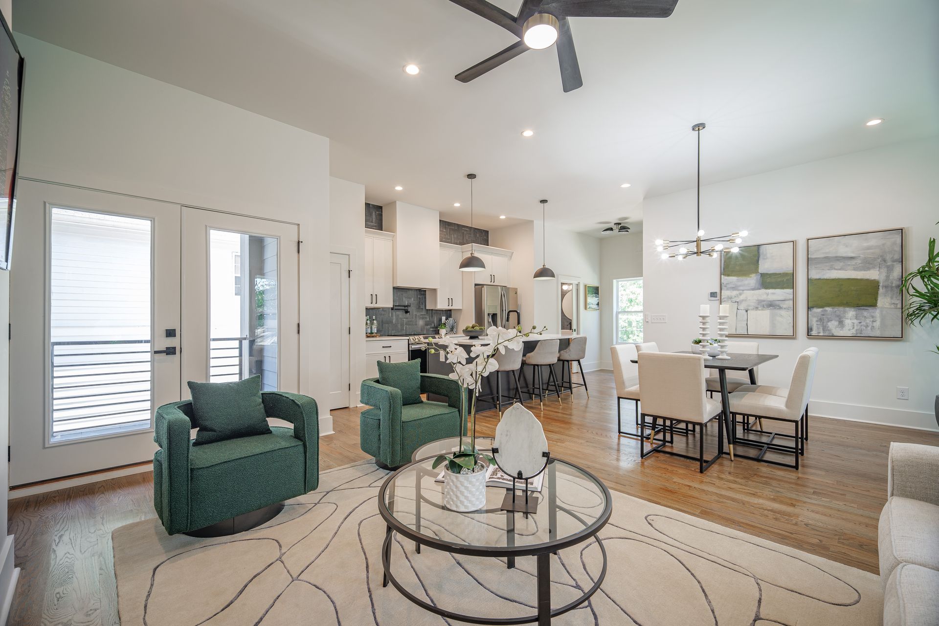Open-concept living space with green armchairs, a glass coffee table, and an open kitchen with bar seating.