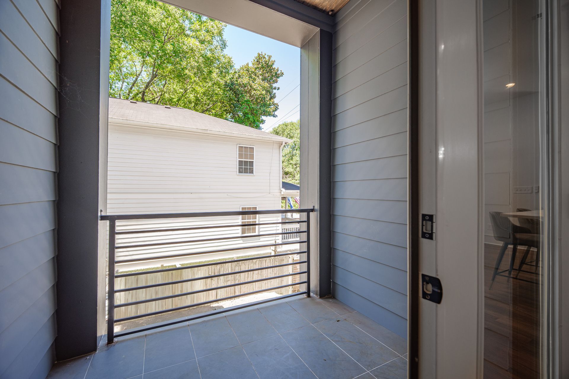 Balcony with a metal railing, overlooking a white house and trees on a sunny day.