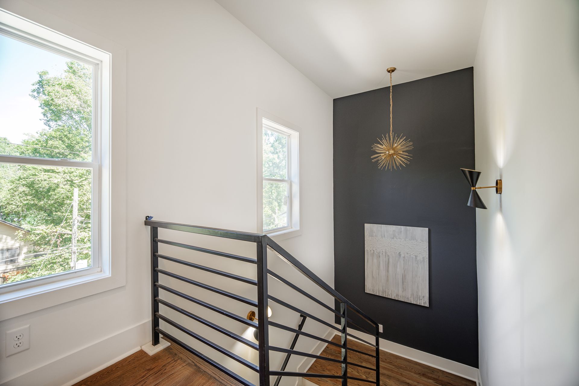 Staircase with black railing, white walls, dark accent wall, gold light fixture, and two windows.