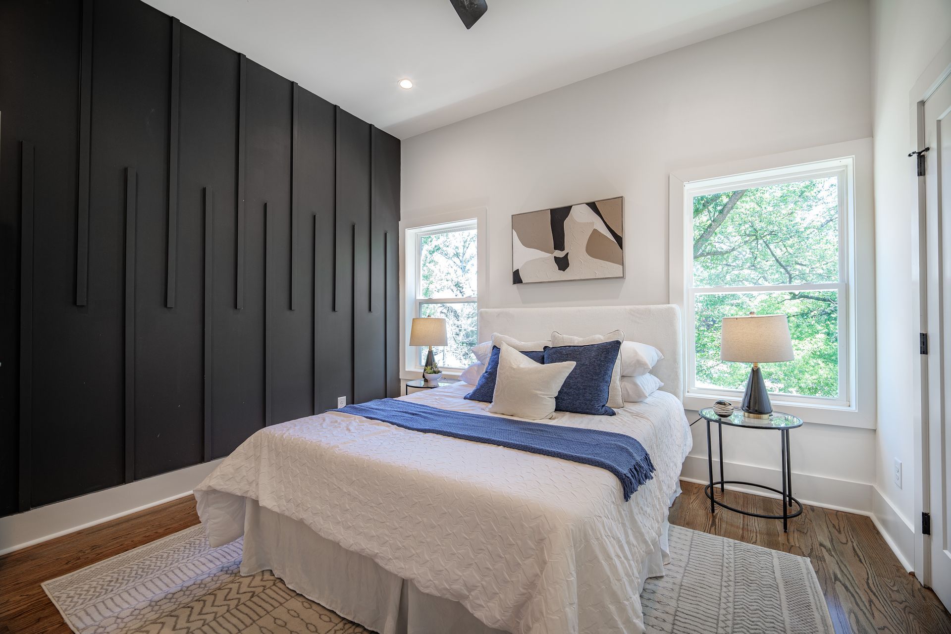 Bedroom with dark accent wall, bed, windows, and bedside tables.