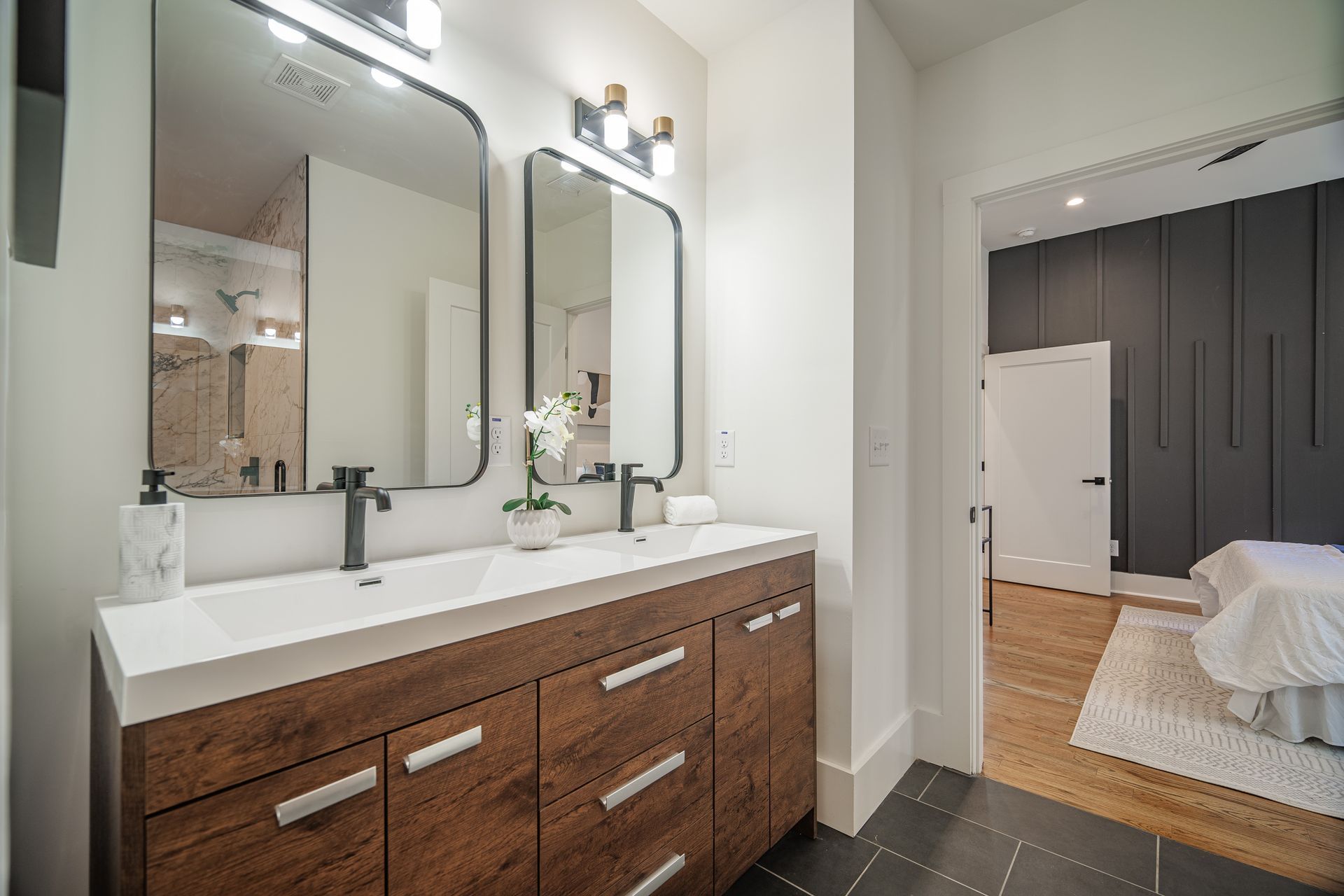 Bathroom with double vanity, two mirrors, and a bedroom visible in the doorway.