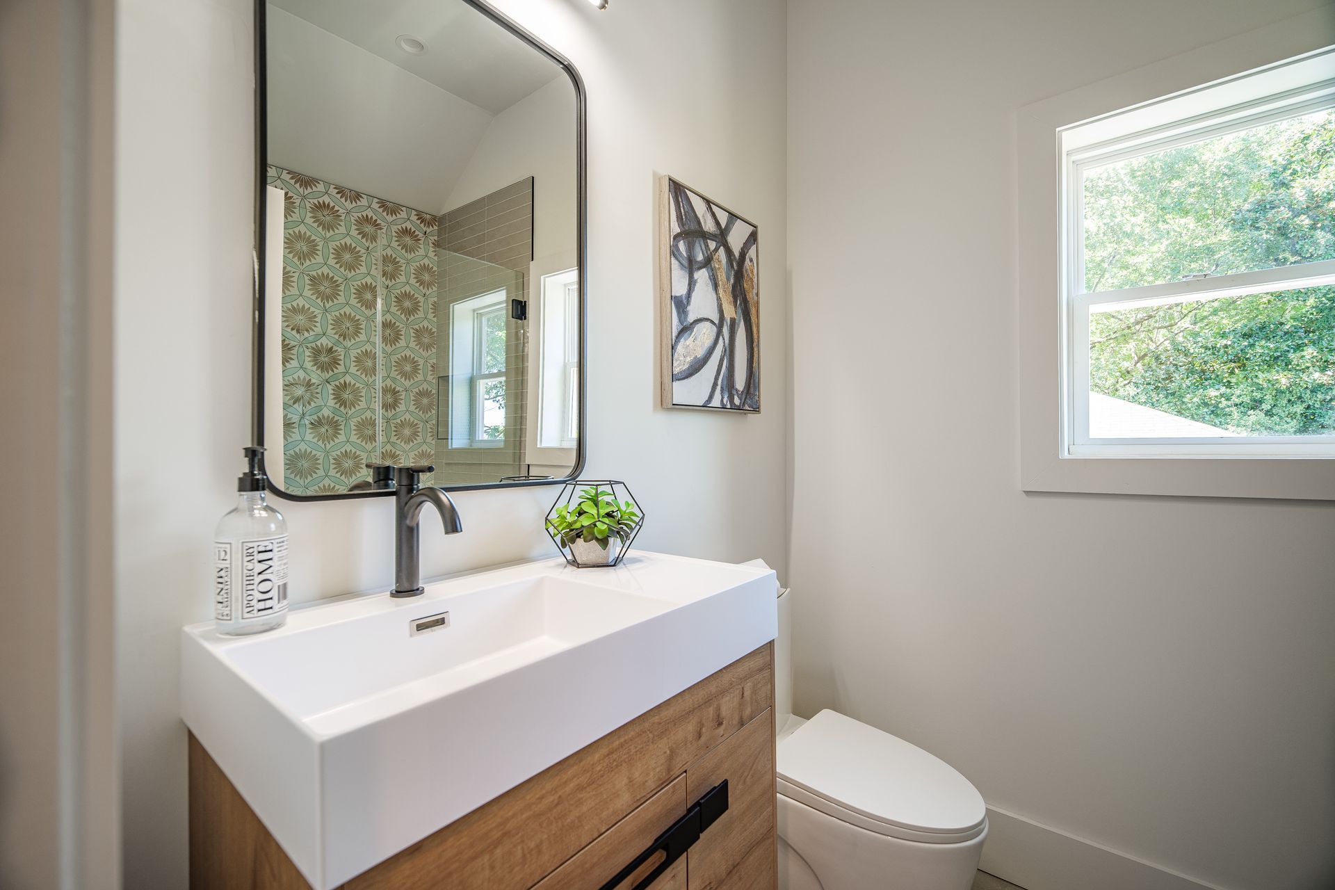 Modern bathroom with white sink, wooden cabinet, black faucet, and patterned shower wall.