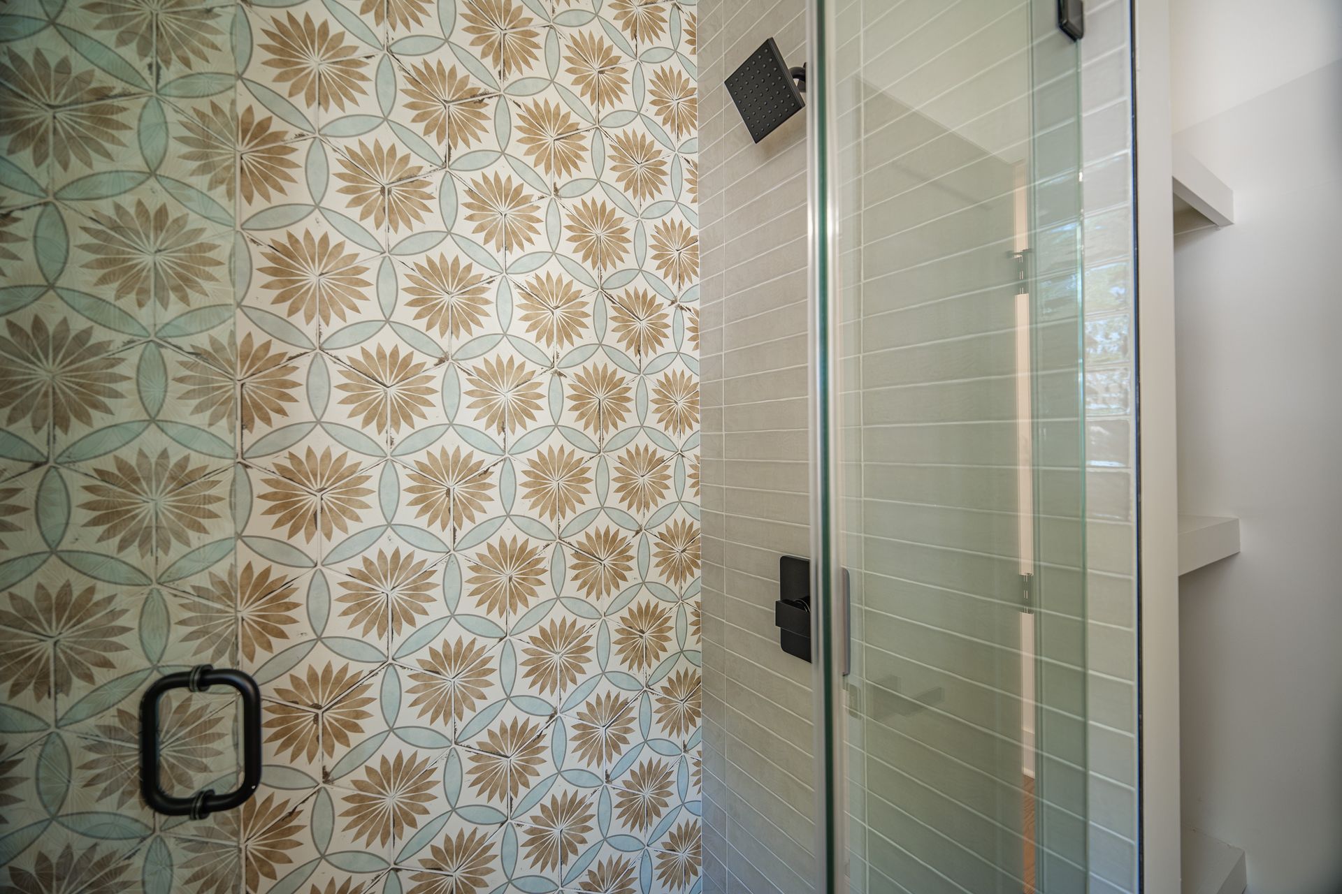 Shower with floral tile wall, glass door, and black hardware.
