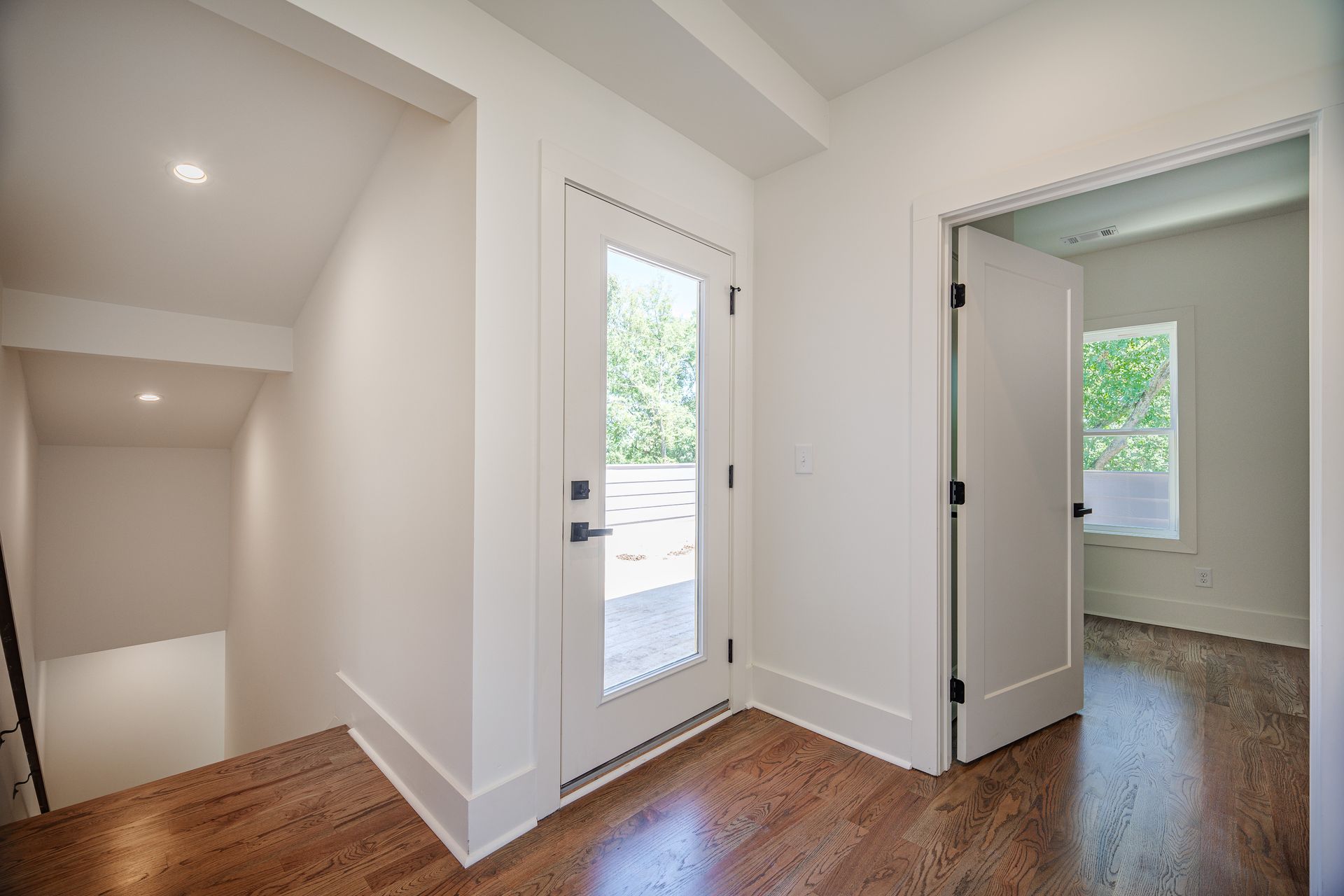 Interior view of a hallway with white walls, wood floors, and a glass-paneled door leading outside.