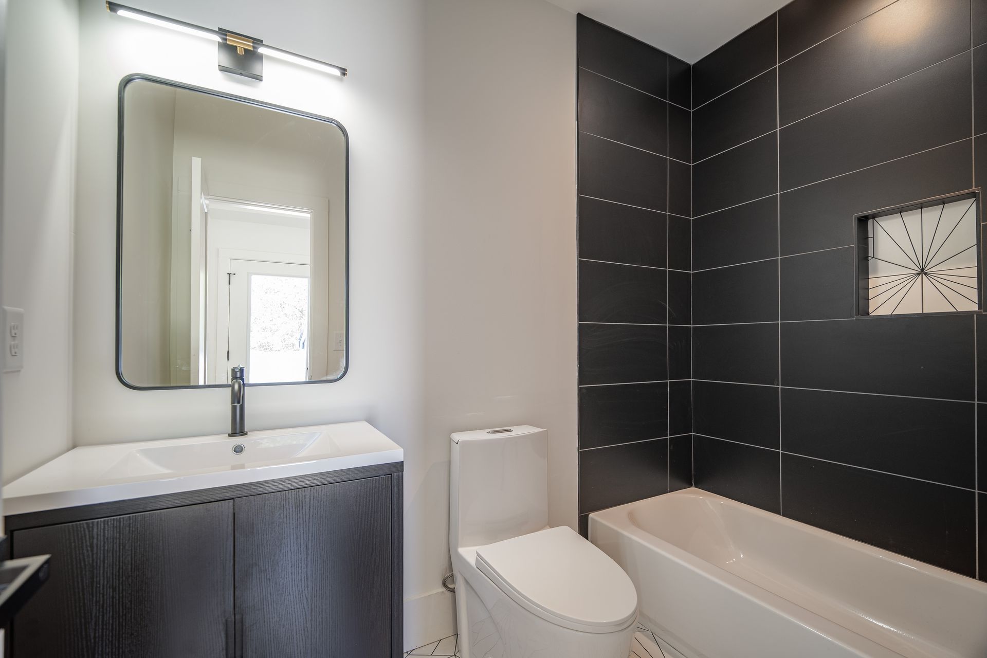 Bathroom with gray vanity, black tiled shower, white toilet, and large mirror.