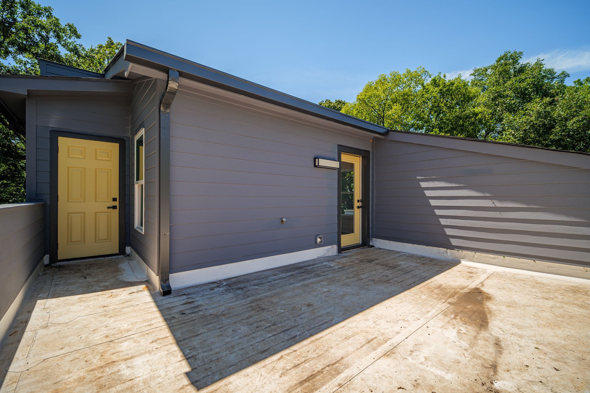 Exterior rooftop patio with gray walls, yellow doors, and blue sky.