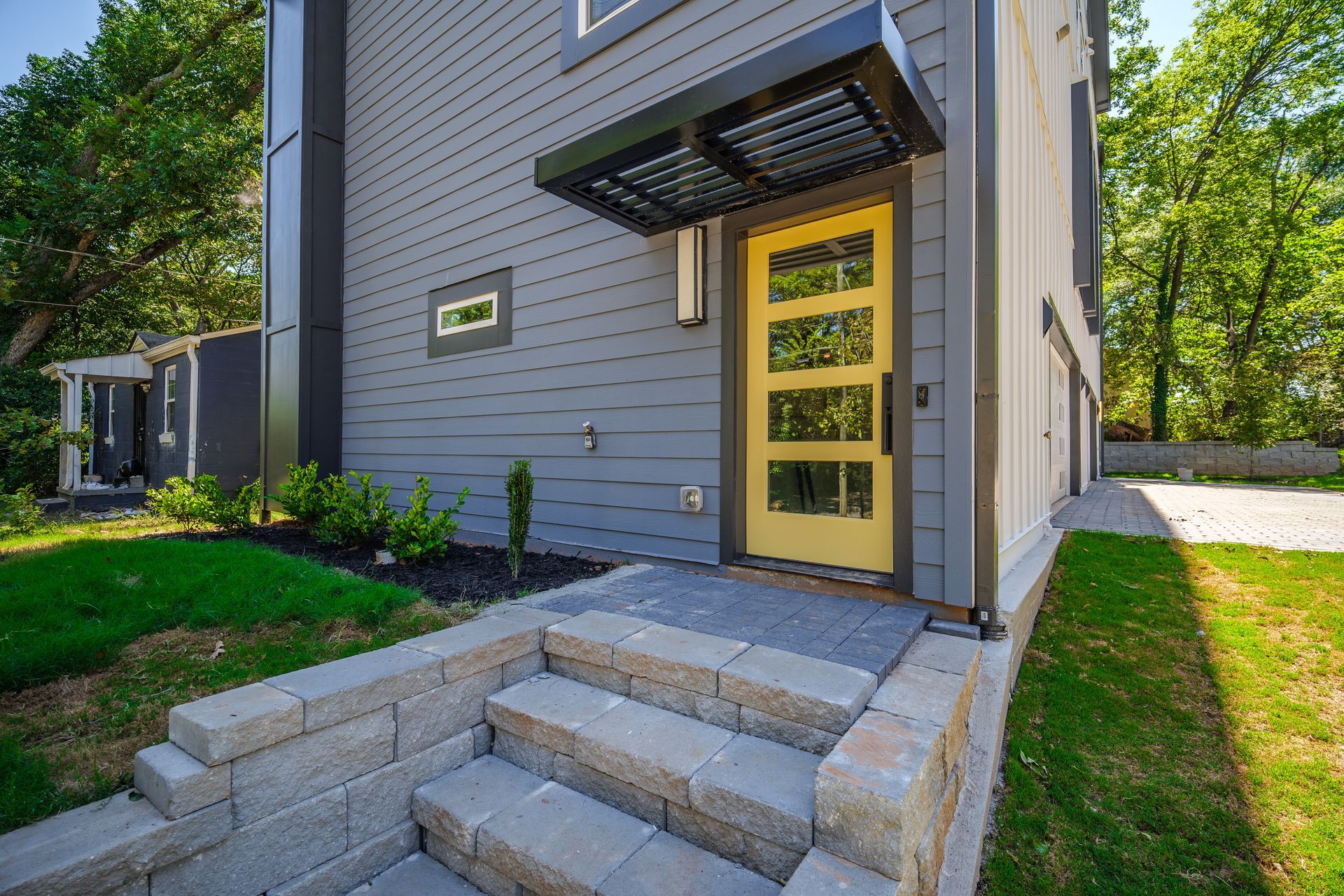 Modern home with yellow door, gray siding, and a black awning over the entrance. Stone steps lead to the door.