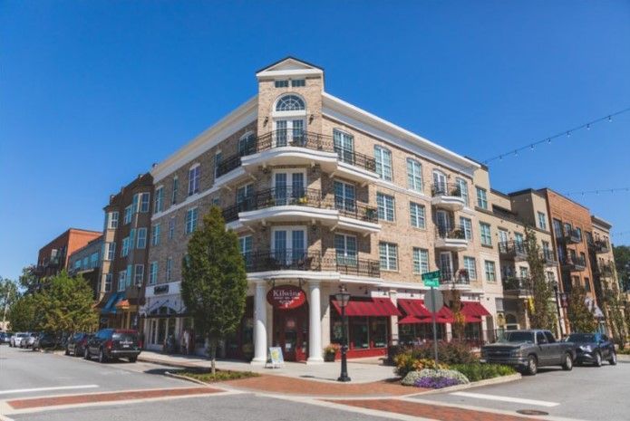 Multi-story brick building with shops on the ground floor, balconies, and a corner entrance; clear blue sky.