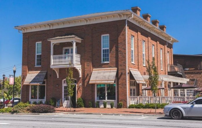 Brick building with white trim, awnings, and a balcony. A car is parked on the street.