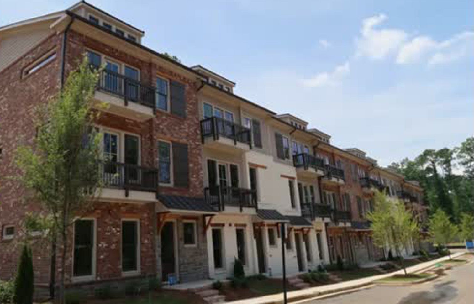 Row of brick and stucco townhouses with balconies and a blue sky.