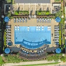 Aerial view of a rectangular pool with lounge chairs, umbrellas, and surrounding landscaping.