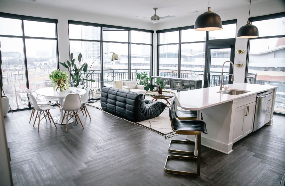 Modern open-plan living space with kitchen island, seating area, large windows, and outdoor balcony.