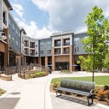 Exterior of apartment complex with benches and walkway on sunny day.