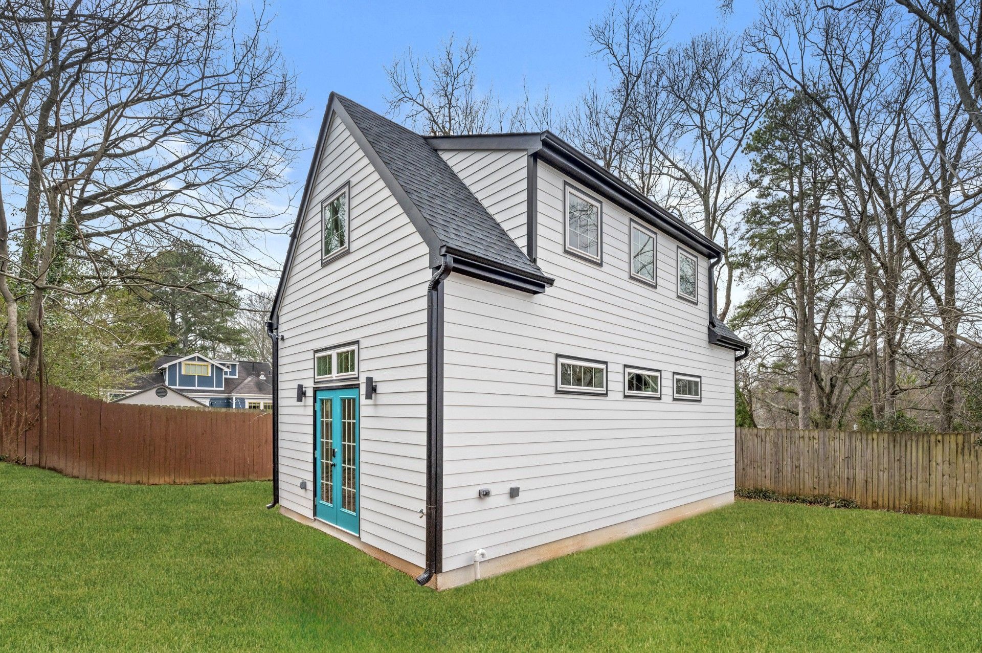 Two-story modern white building with black trim and teal doors, surrounded by green grass and trees.