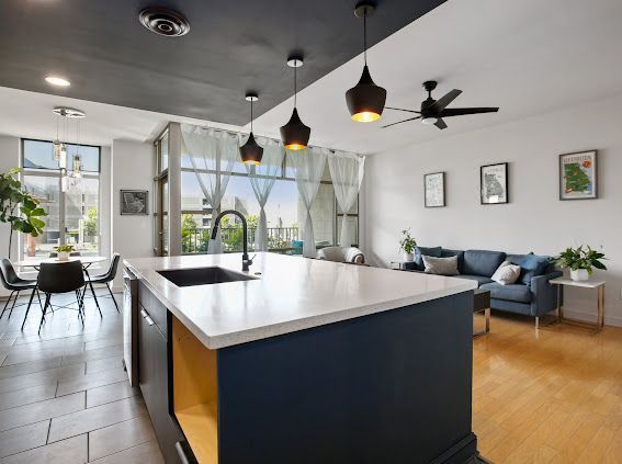 Modern open-plan kitchen and living room with island, dark blue cabinets, and a white countertop.