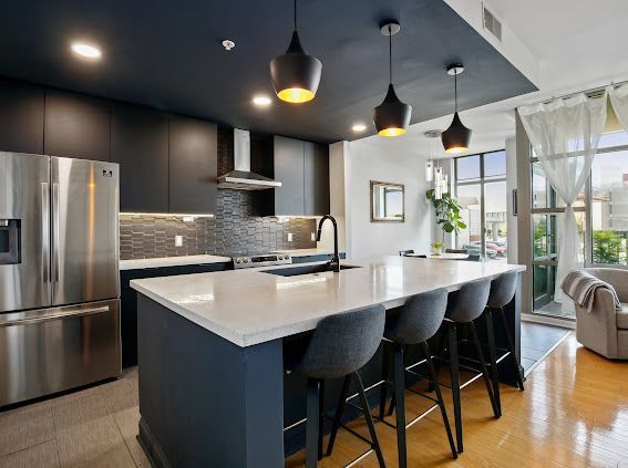 Modern kitchen with a dark blue island, stainless steel appliances, and pendant lights.