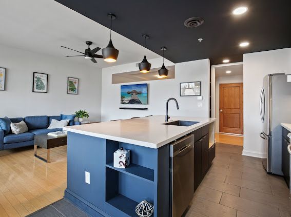 Modern kitchen and living space, blue and white, with island and sofa.