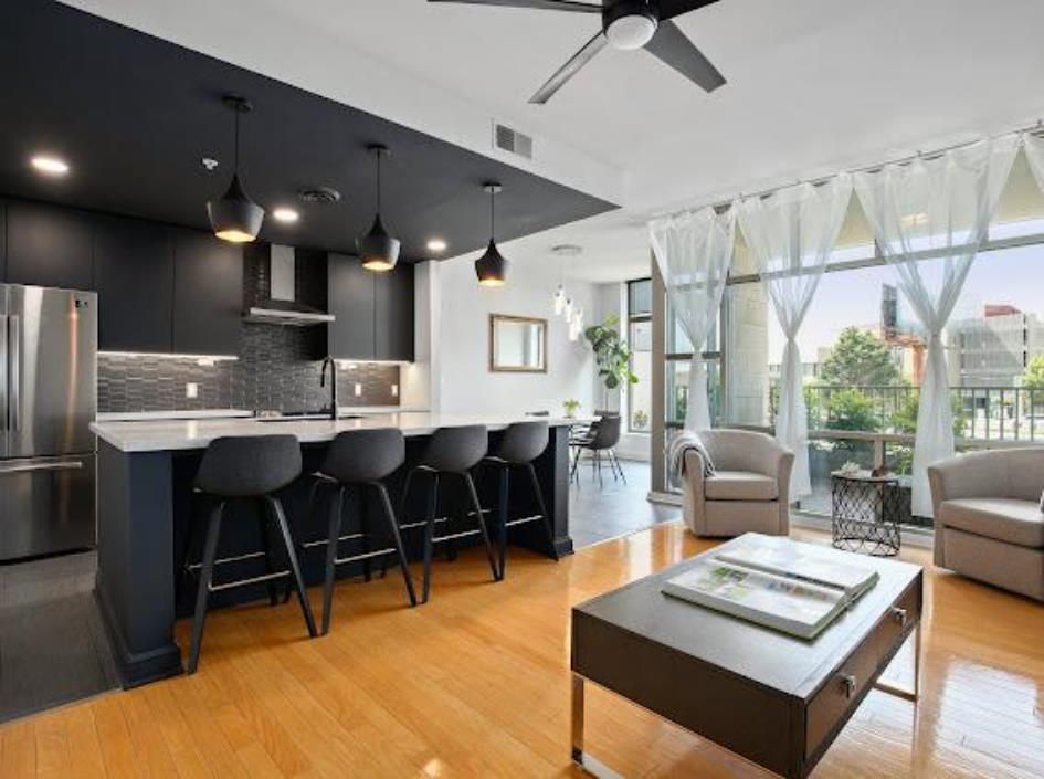 Modern kitchen and living space with dark blue cabinets, island with stools, and balcony view.