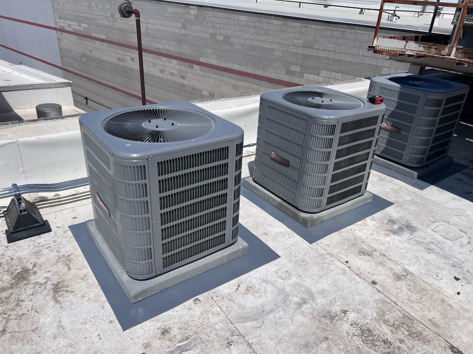 Three gray air conditioning units on a white rooftop.