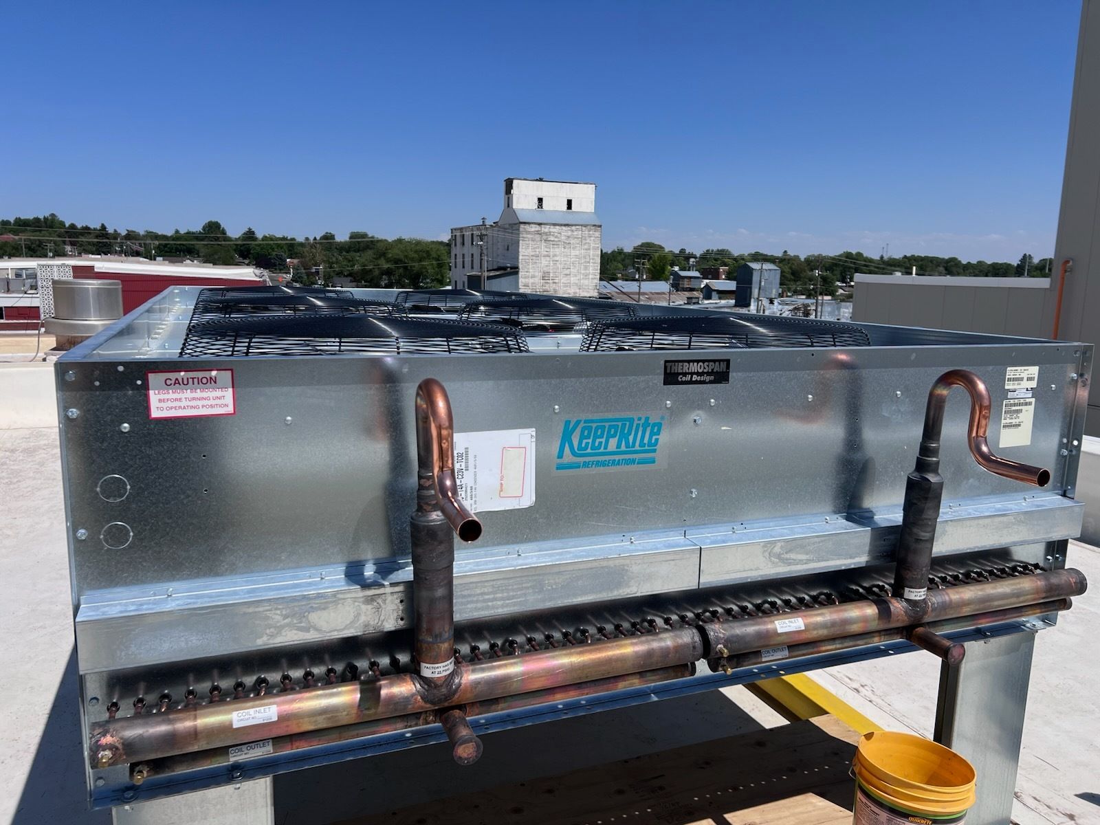 Rooftop HVAC unit with copper pipes and fans, under a clear blue sky.