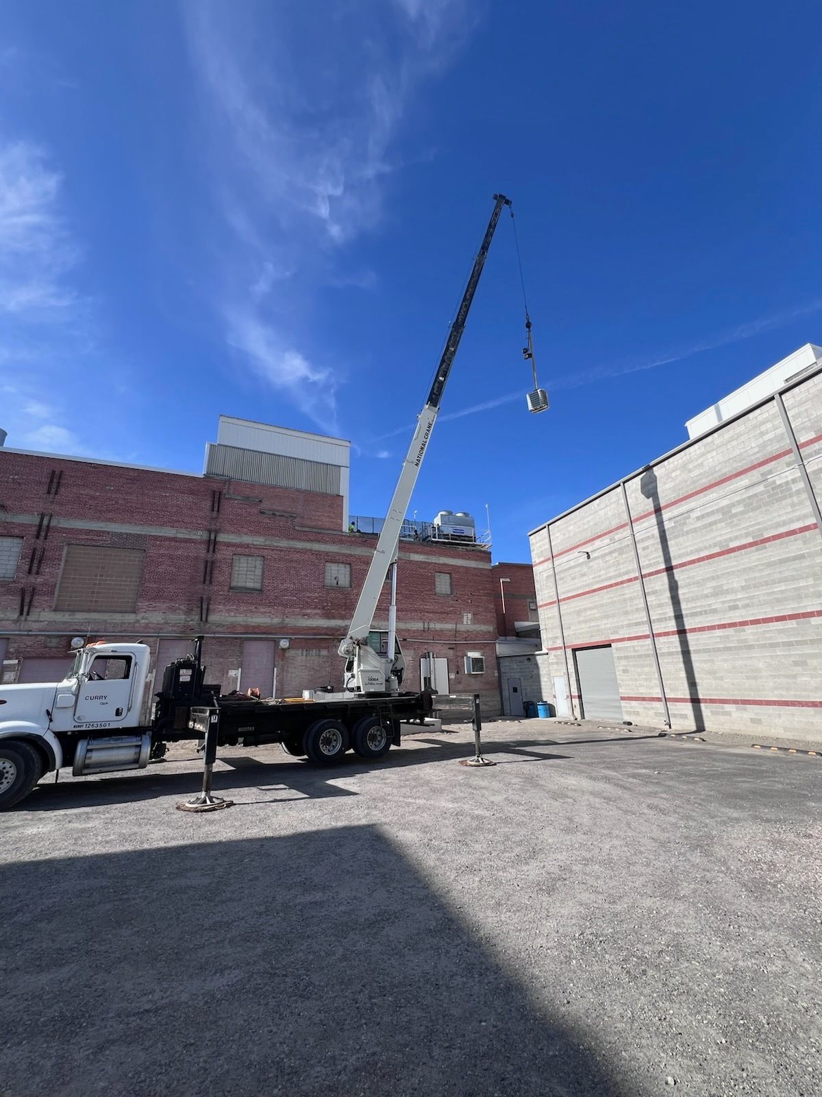 A crane lifting an object near two buildings. Bright blue sky overhead.