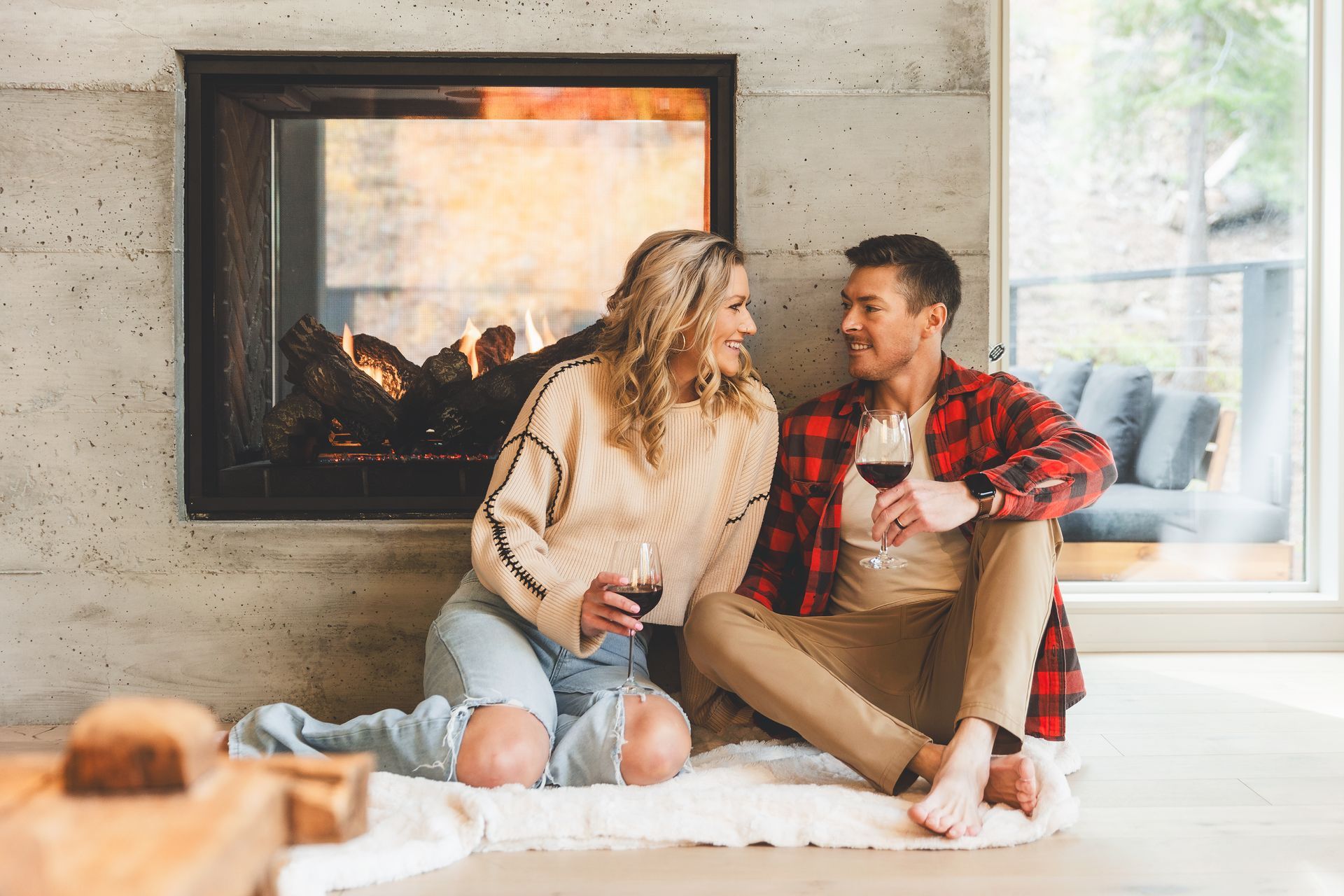 Couple sitting on a rug by a fireplace, smiling and talking in a cozy living room
