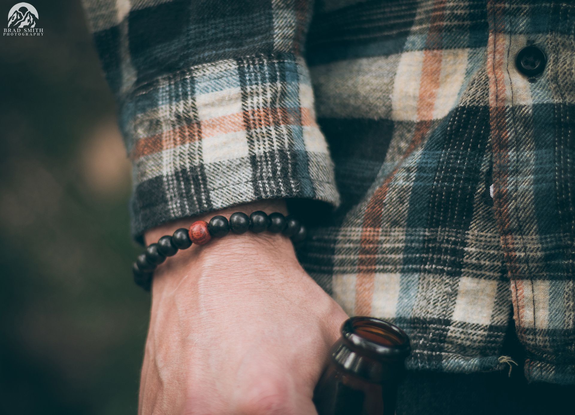 Close-up of a hand in a plaid flannel shirt holding a bottle, with beaded bracelets.