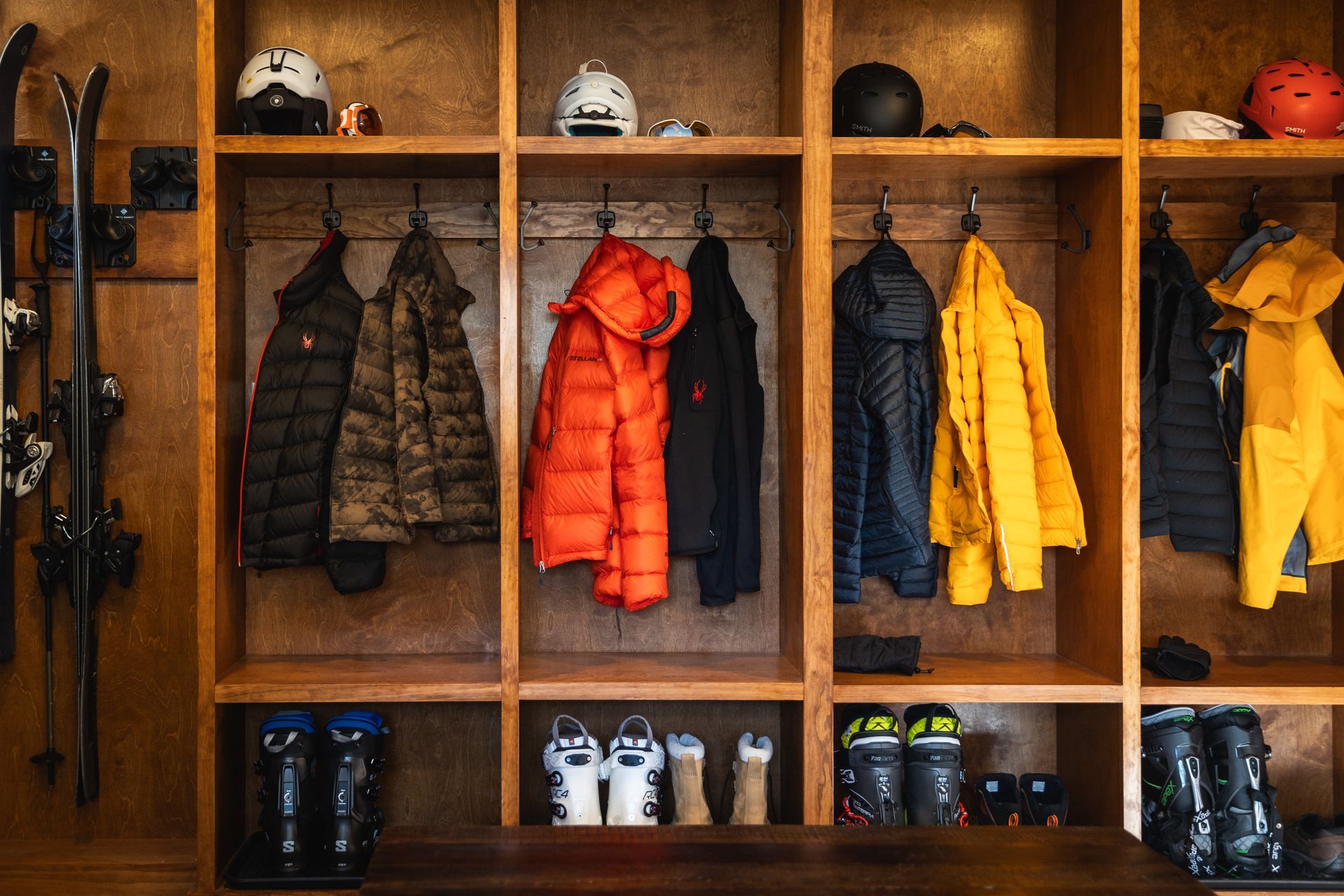 Wooden coat rack with winter jackets, helmets, gloves, and boots in cubbies