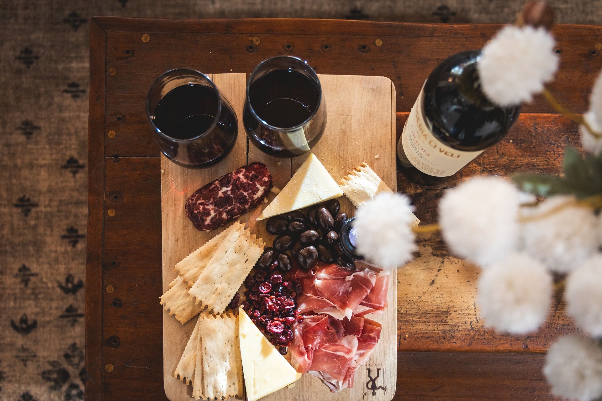 Wooden board with cheese, grapes, crackers, and two glasses of red wine