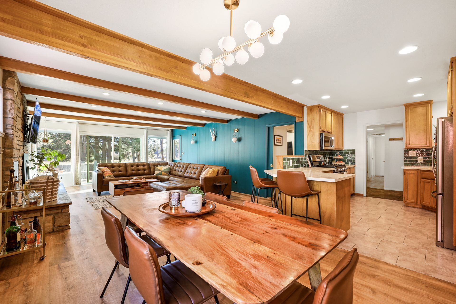 Open-plan kitchen and dining area with wood beams, teal accent wall, and warm wood furnishings