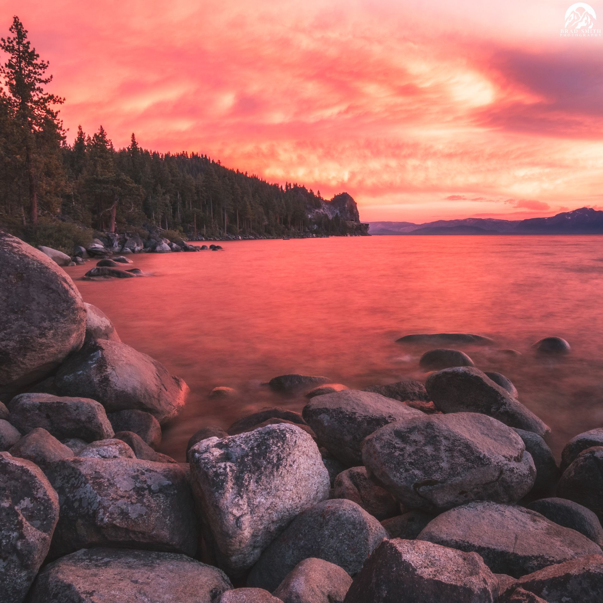 Rocky lakeshore at sunset with pink clouds reflecting on calm water