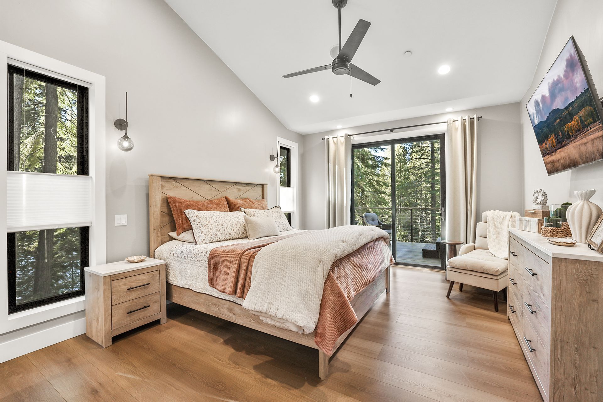 Bright modern bedroom with wood bed, white bedding, large windows, ceiling fan, and dresser by the wall