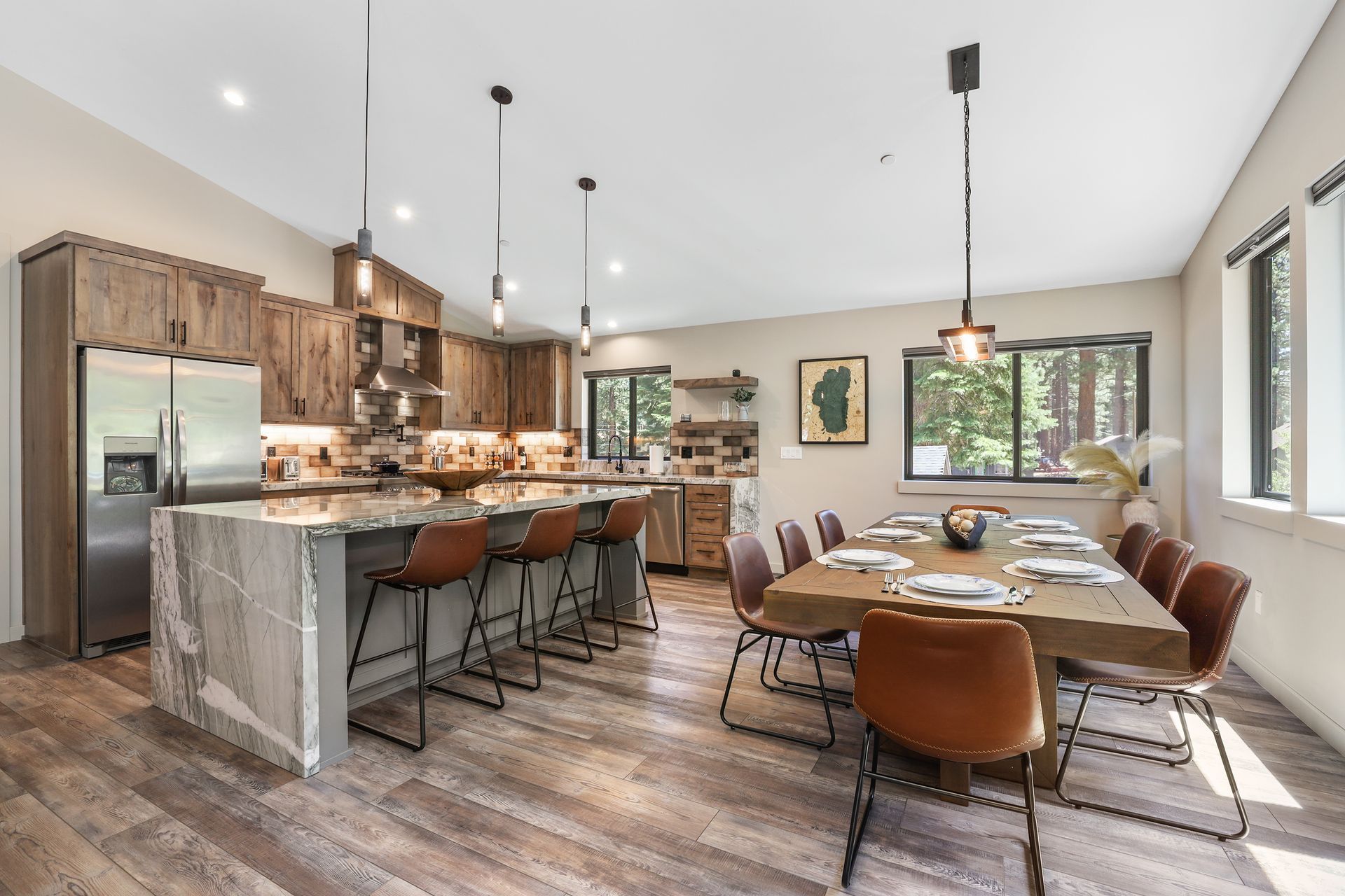 Modern kitchen and dining area with marble island, brown chairs, wood floors, and large windows