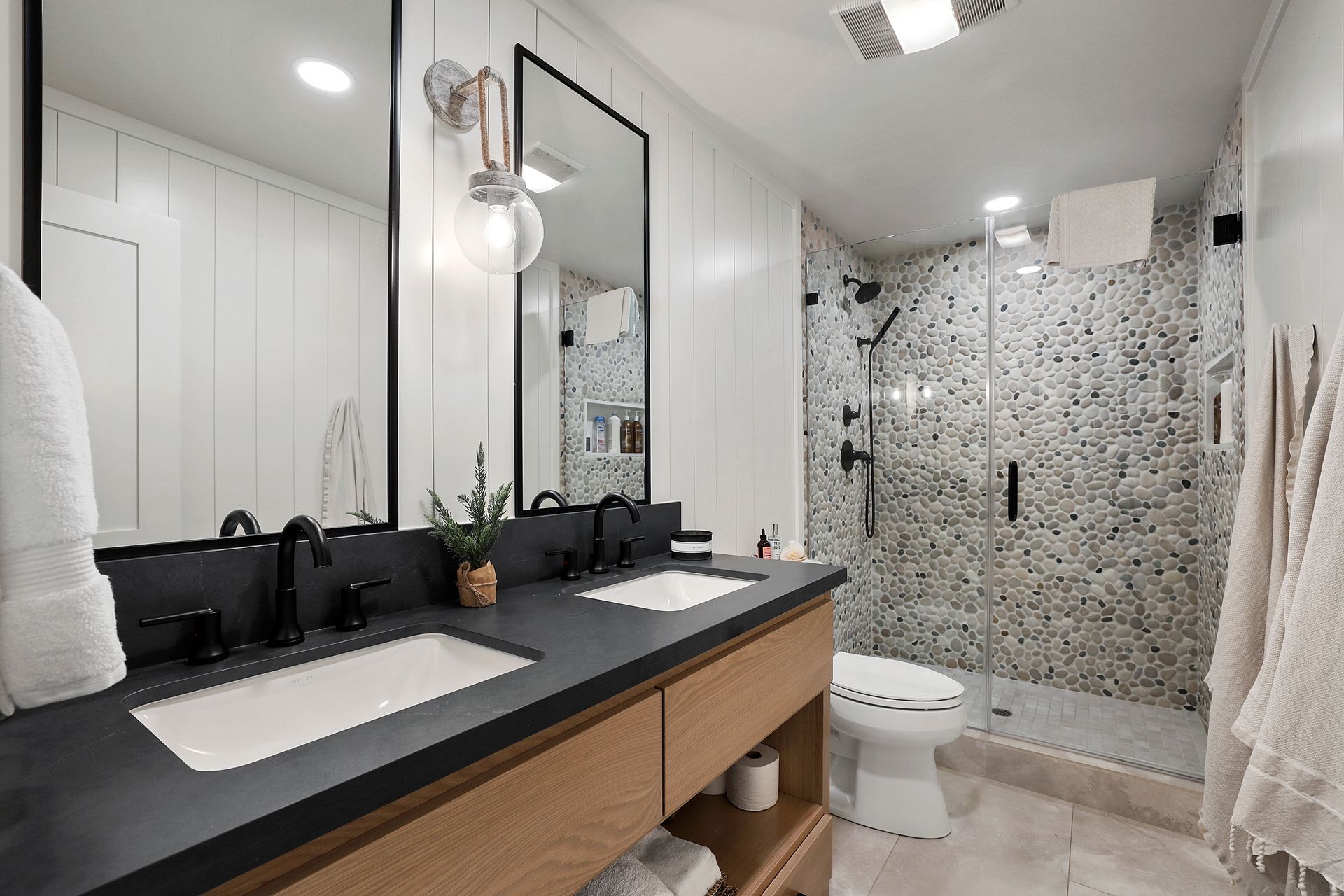 Modern bathroom with black vanity, white sink, mirror, and mosaic-tile walk-in shower