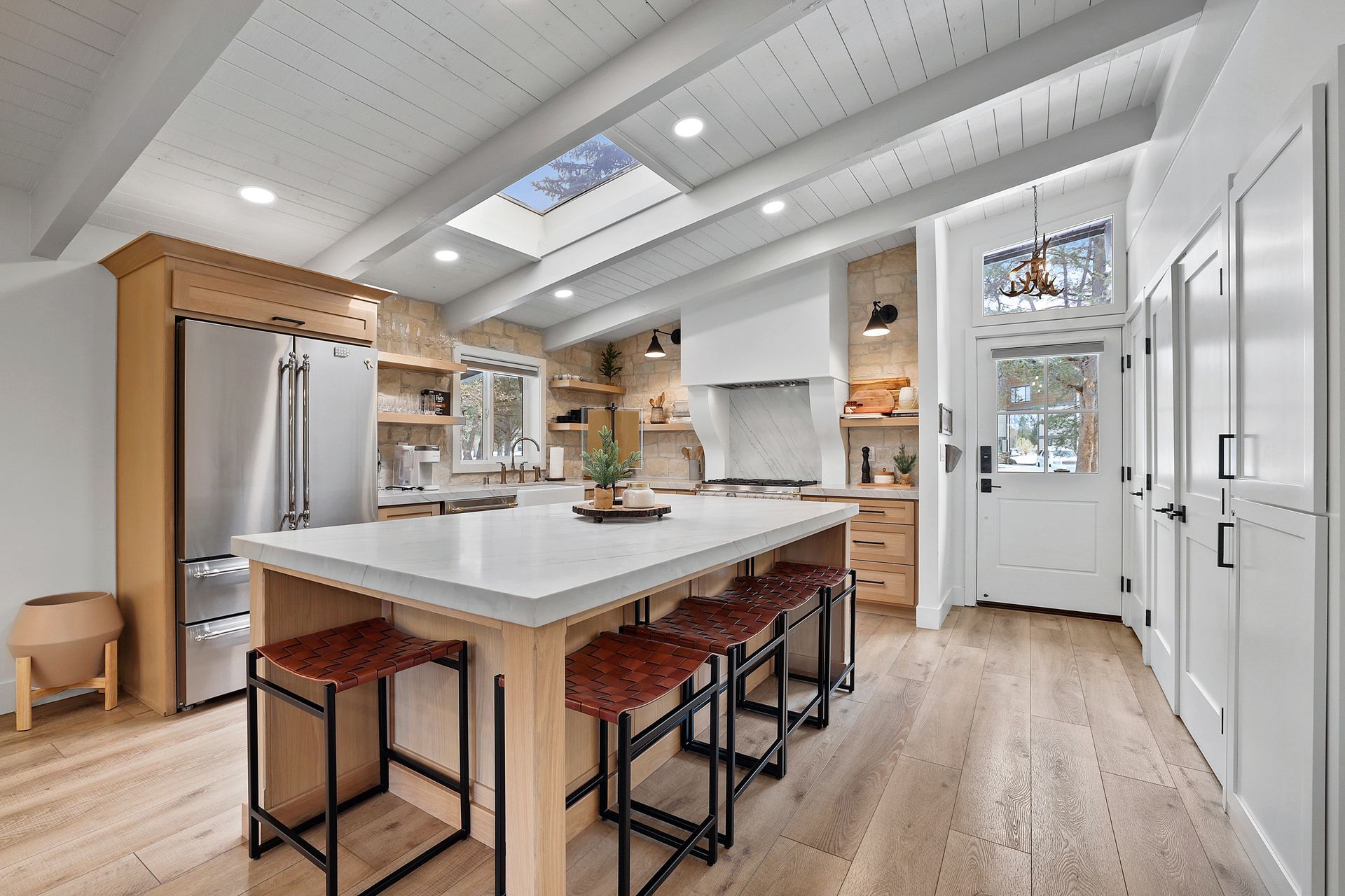Bright modern kitchen with large island, white cabinets, wood floors, and skylight.