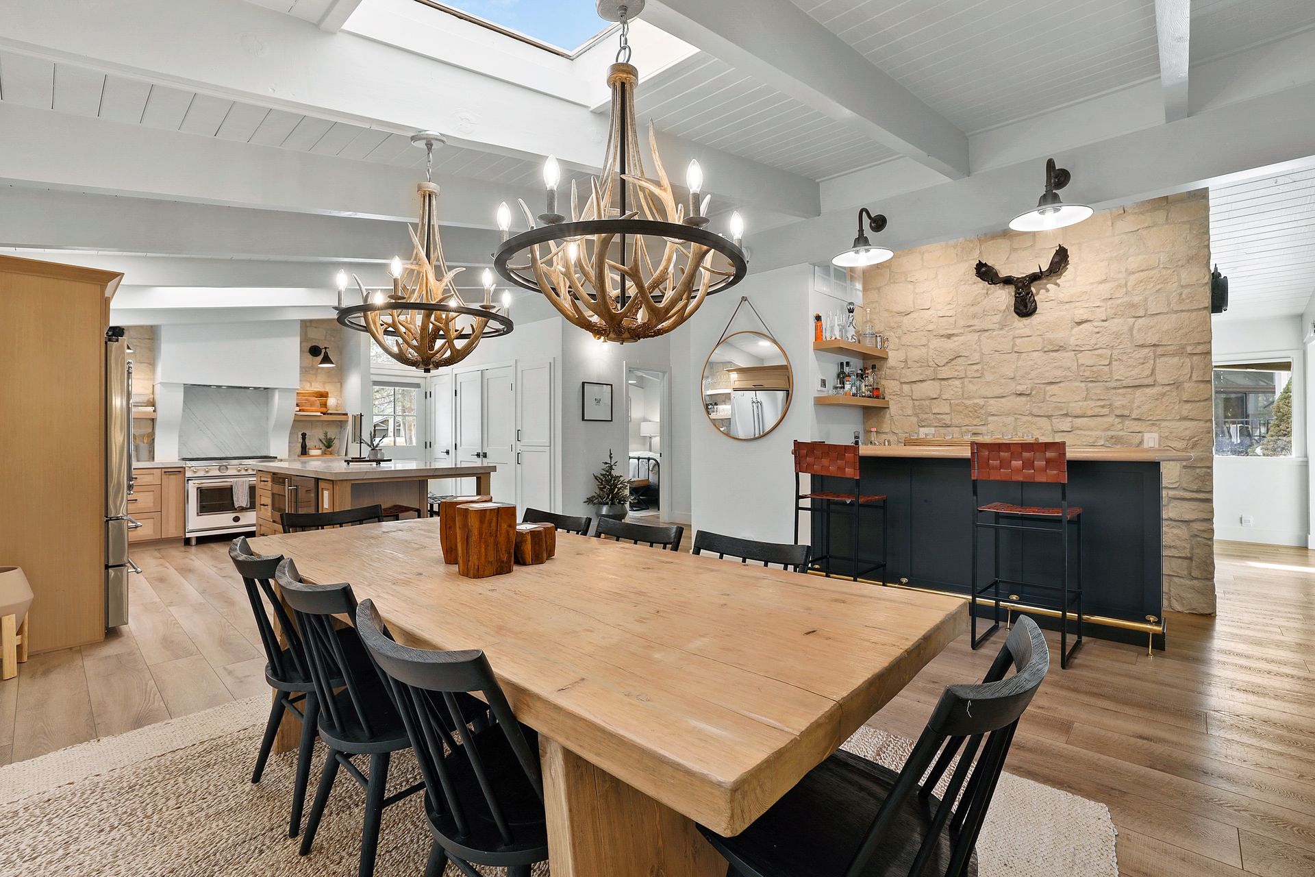 Spacious dining room with a large wood table, black chairs, chandeliers, and a brick fireplace mantel