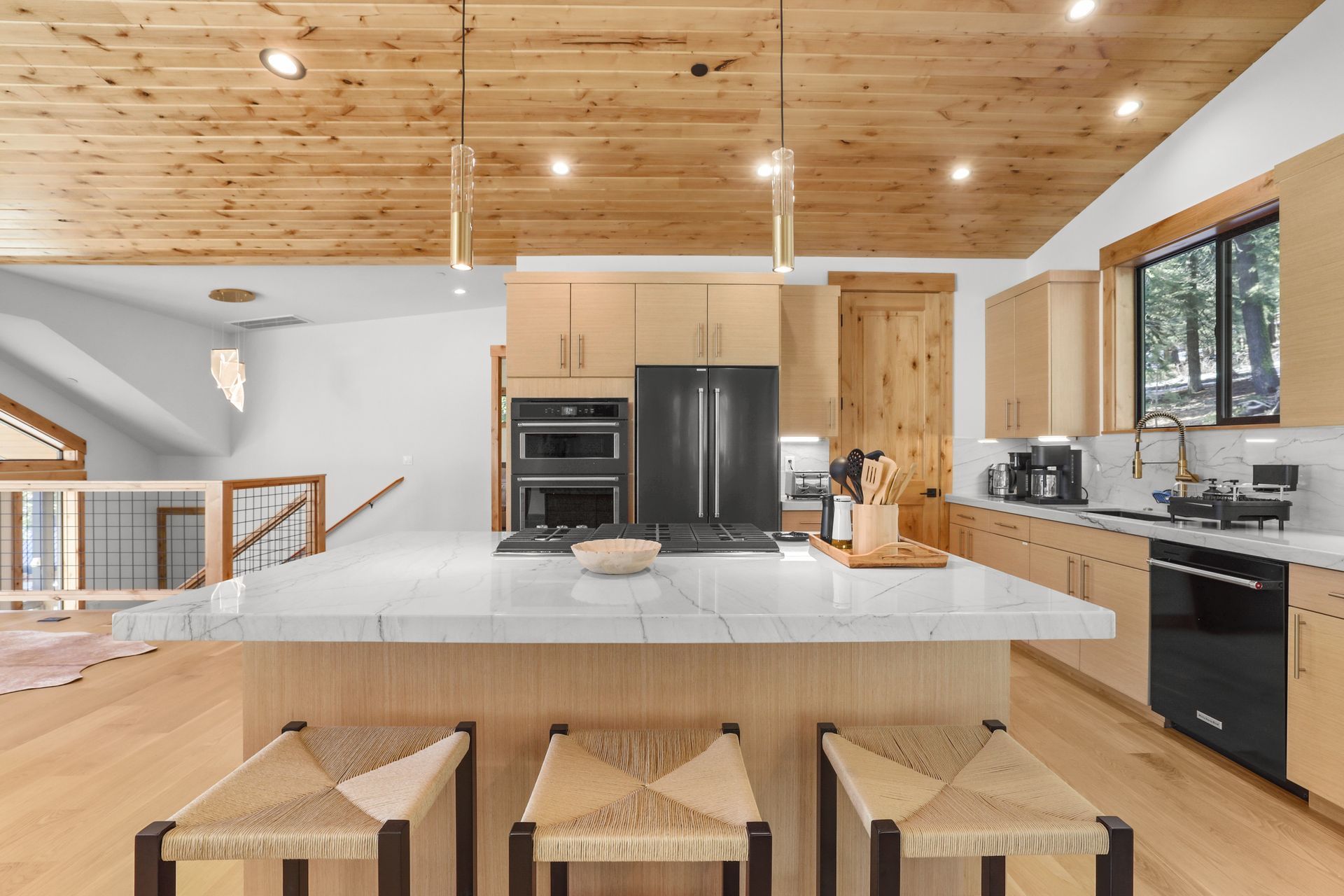 Modern kitchen with large island, wood ceiling, black appliances, and barstools in a bright open space