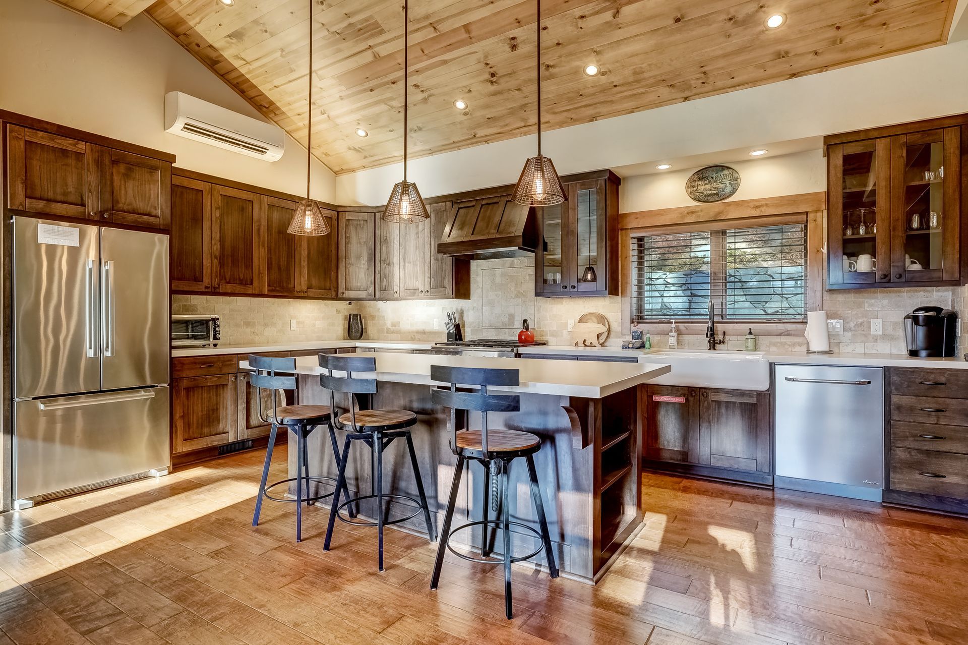 Modern kitchen with stainless steel appliances, wood cabinets, island seating, and pendant lights
