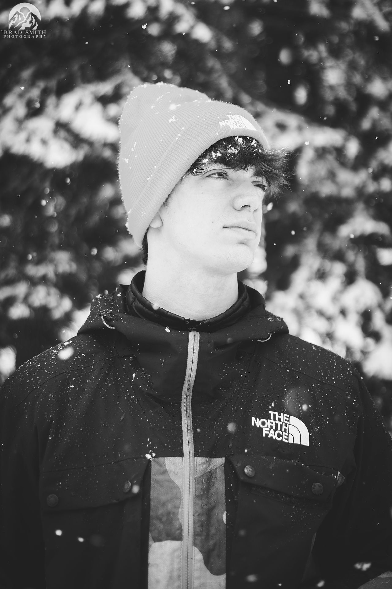 Person in a beanie and North Face jacket standing in falling snow, looking off to the side.