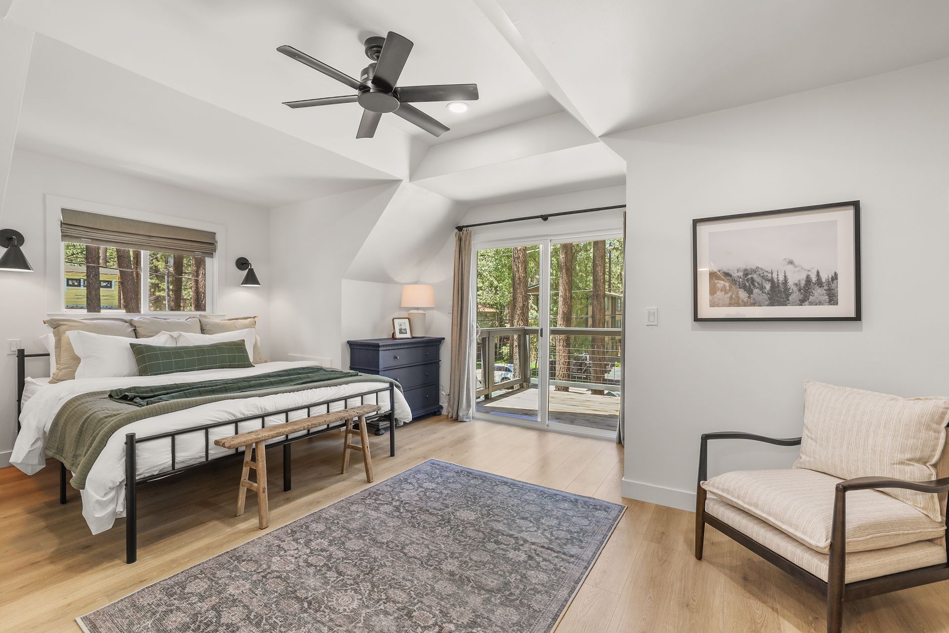 Bright bedroom with a bed, bench, chair, rug, ceiling fan, and sliding doors to a patio.