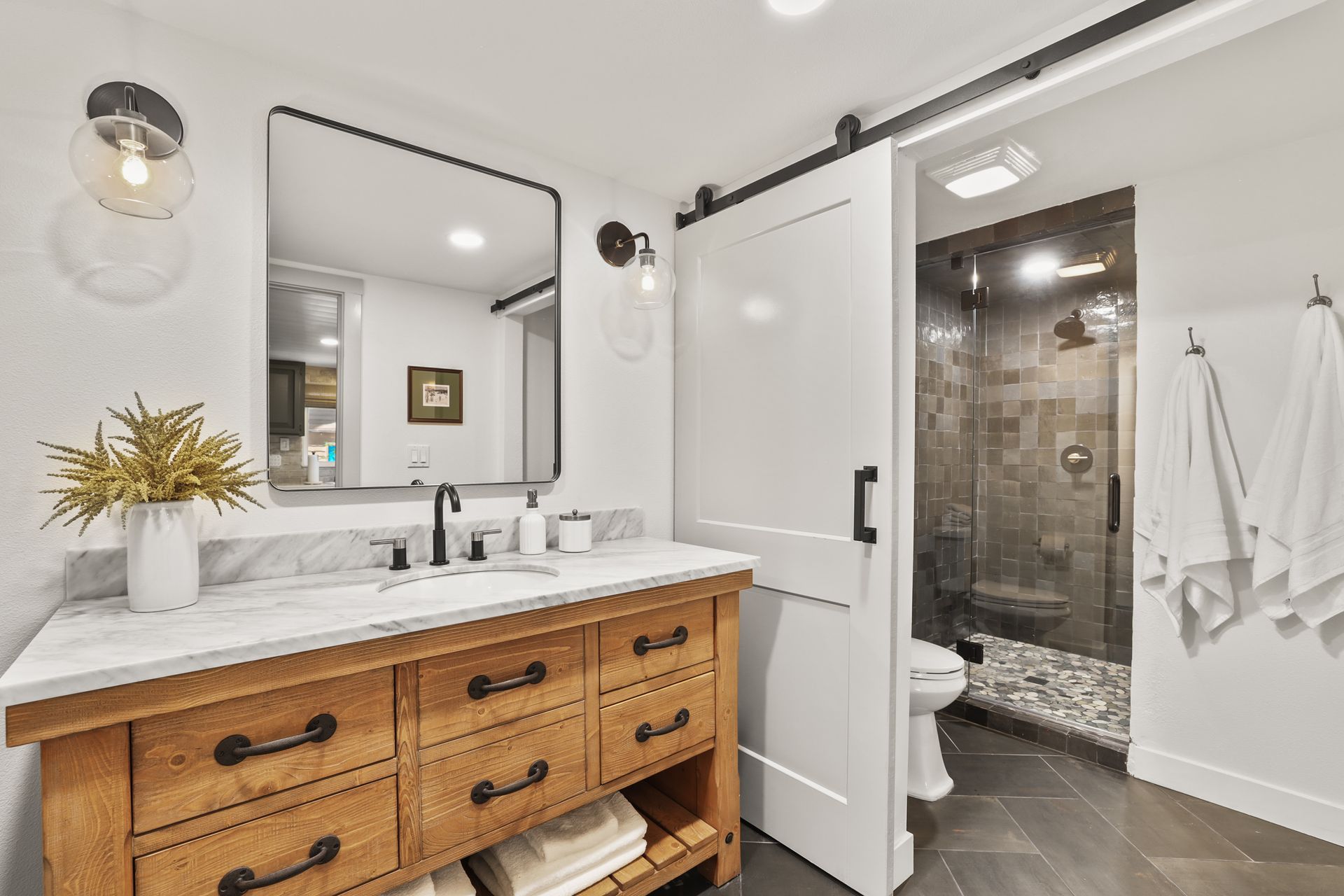 Bathroom vanity with wood cabinet, white sink, large mirror, and open shower door.