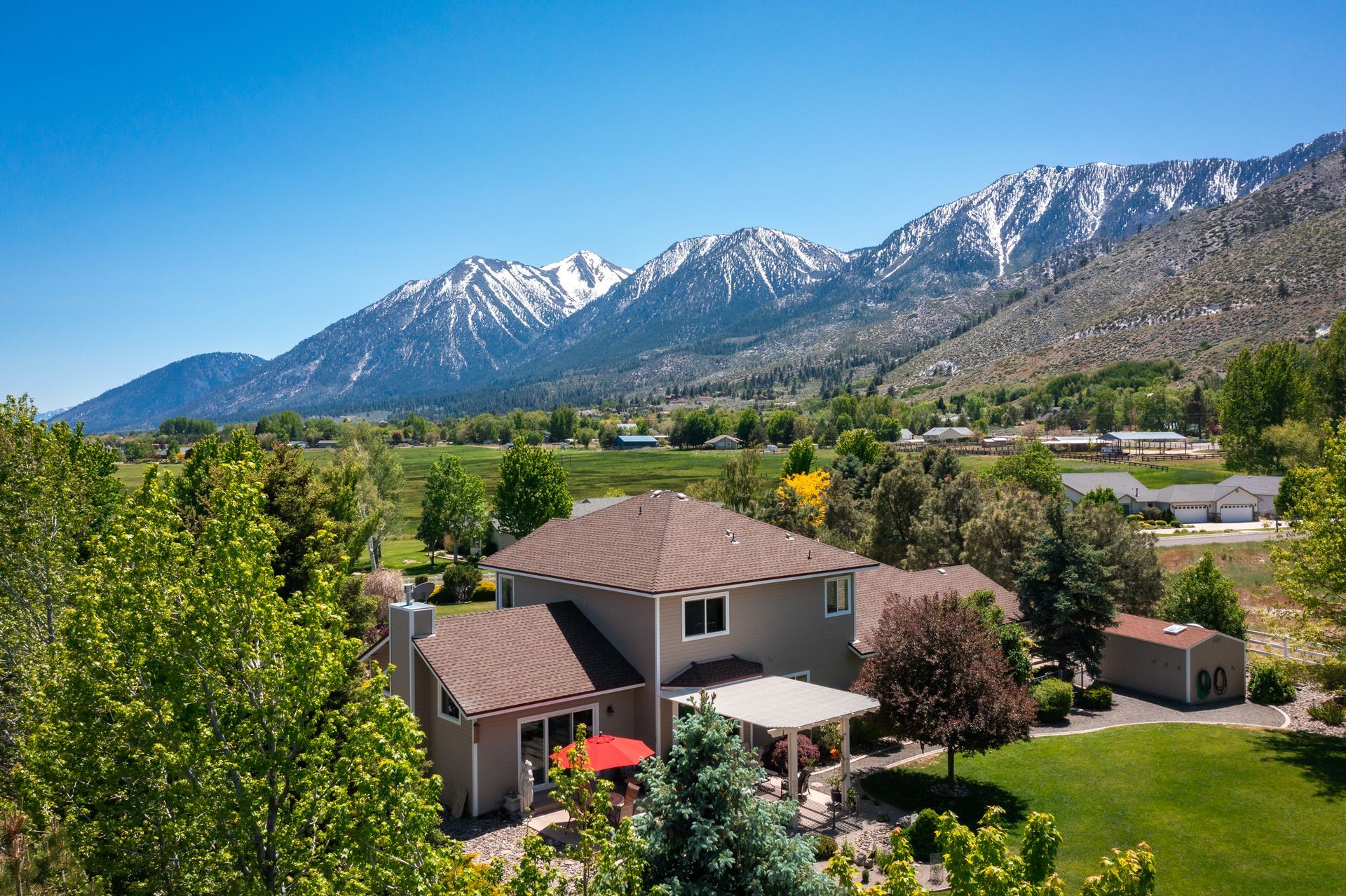 Mountain house with a red umbrella, green trees, and snowy peaks in the background