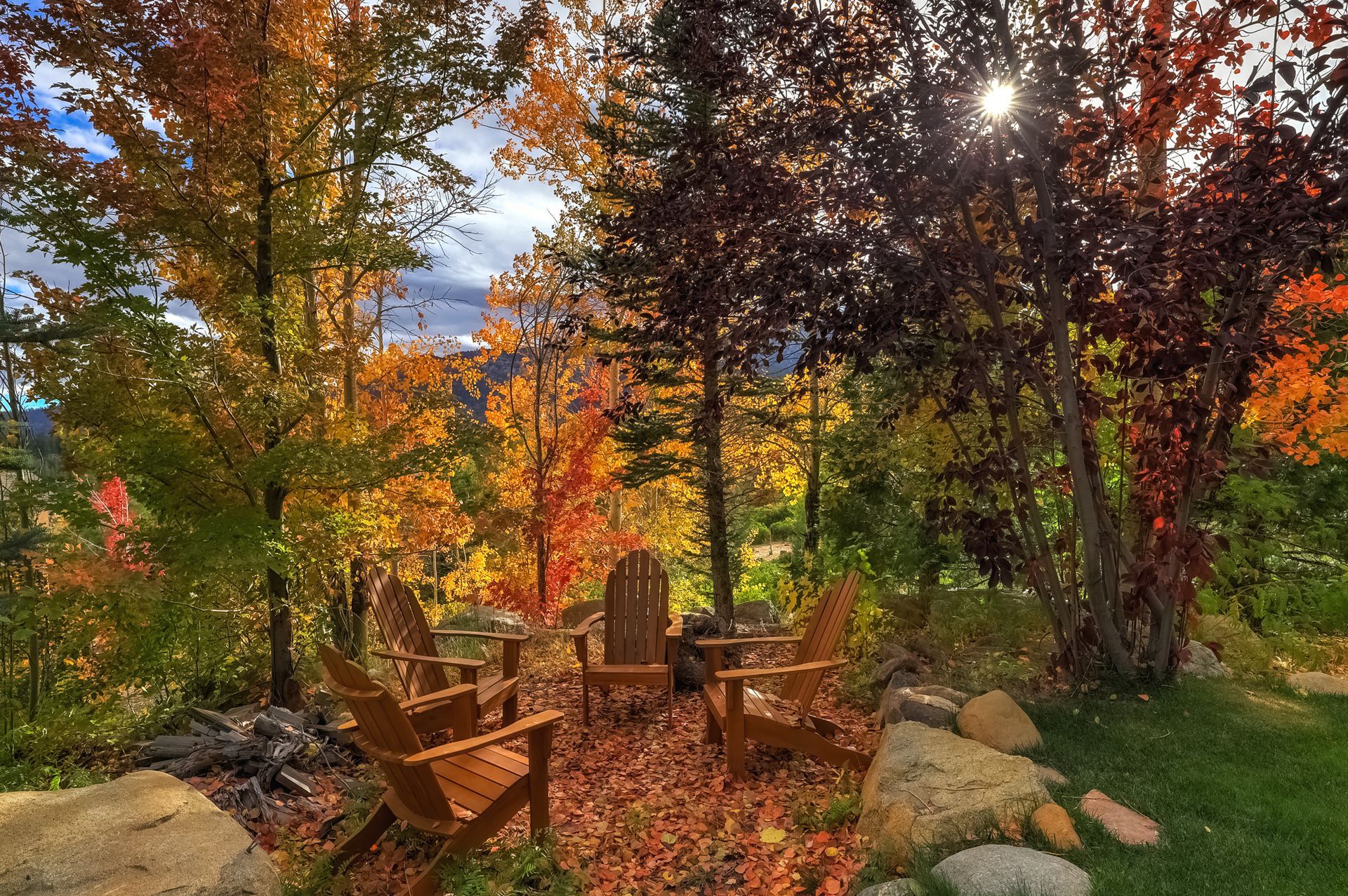 Autumn garden with wooden chairs around a fire pit under colorful trees and sunlight