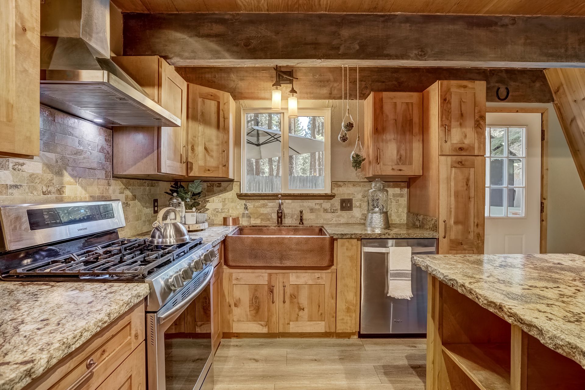 Rustic kitchen with wood cabinets, granite counters, gas stove, sink, and pendant light, viewed from the center