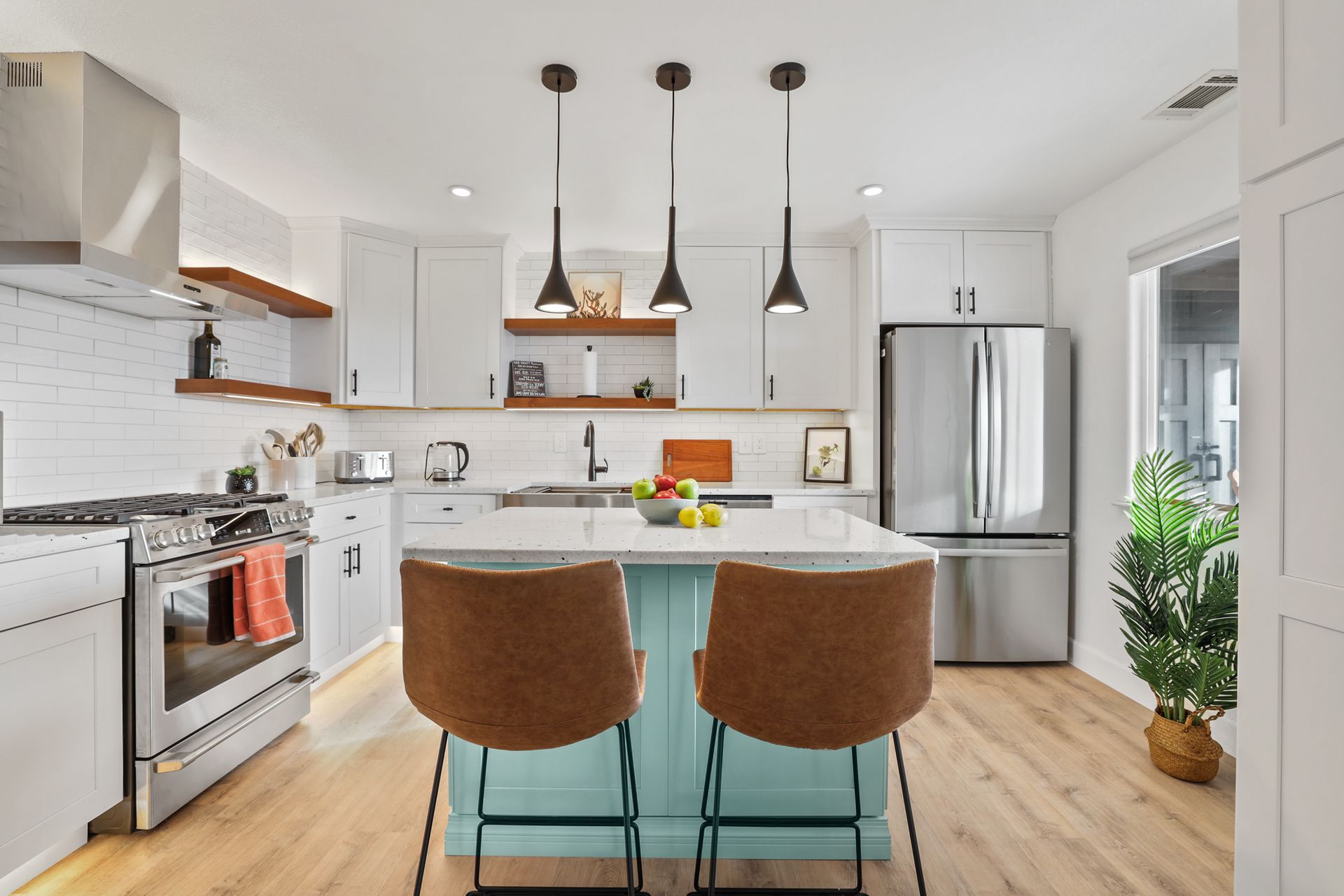 Bright modern kitchen with white cabinets, stainless appliances, island, pendant lights, and two brown stools