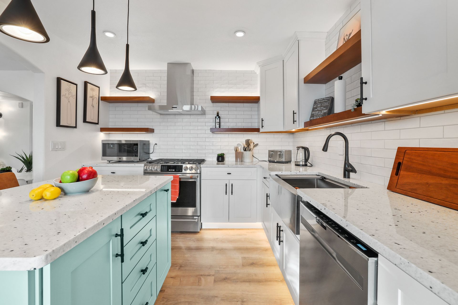 Bright modern white kitchen with mint island, black pendant lights, stainless appliances, and wood floors