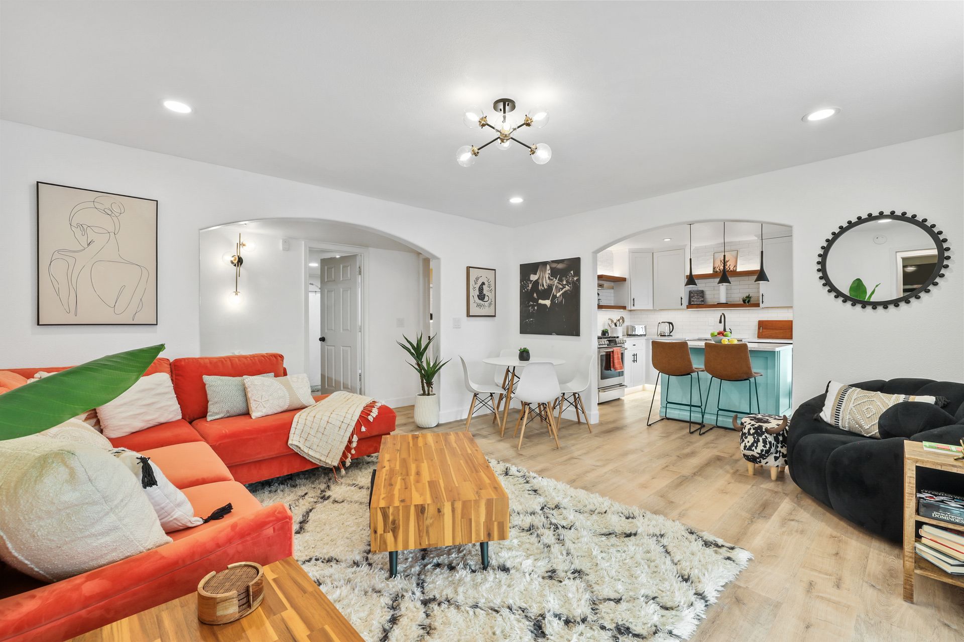 Bright open-plan living room with orange sofa, patterned rug, wood coffee table, and teal kitchen stools