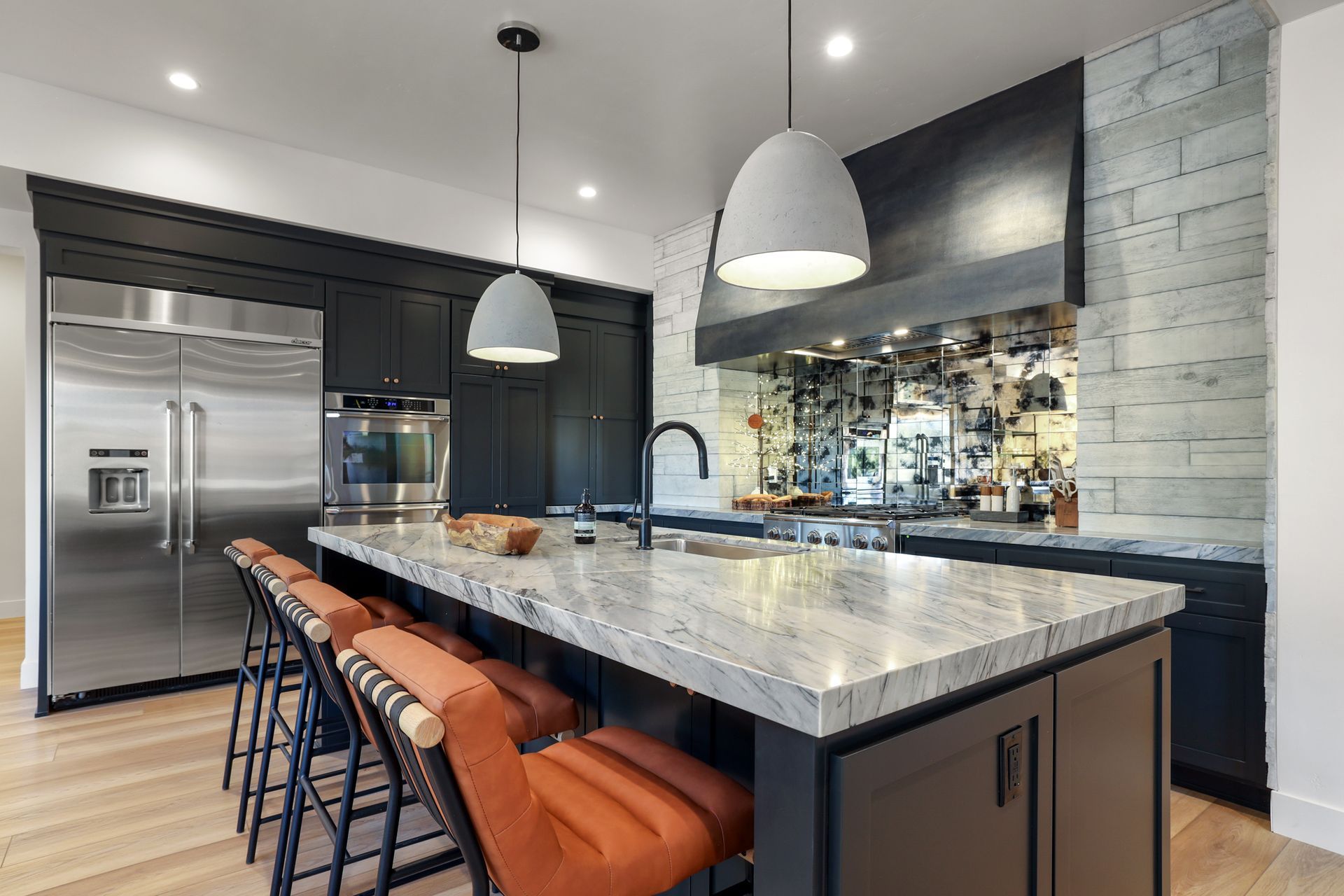 Modern kitchen with a large marble island, pendant lights, black cabinetry, and orange barstools