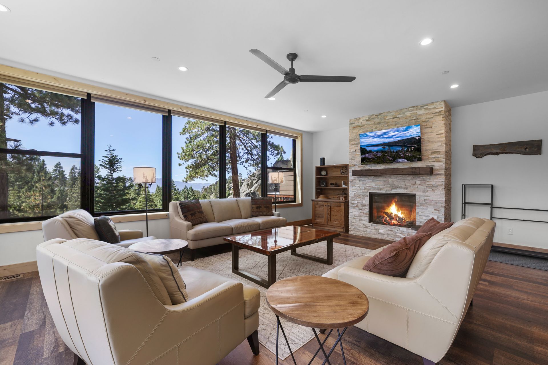 Modern living room with stone fireplace, large windows, beige seating, and mountain views